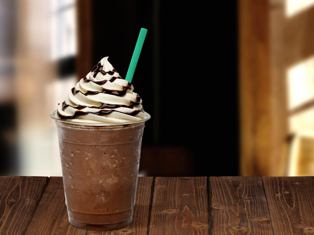 A frappuccino with whipped cream and chocolate drizzle on a wooden counter